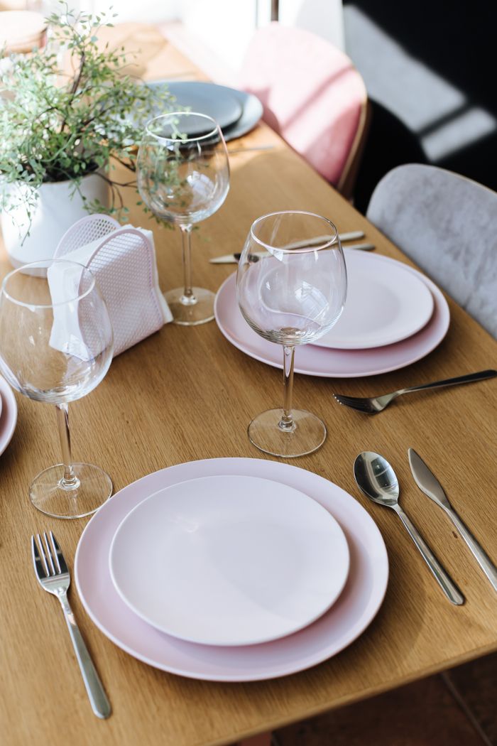 Beautifully arranged dining table with pink plates, cutlery, and wine glasses.